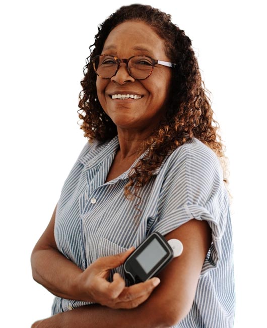 A woman wearing glasses and a striped shirt smiles while holding a glucose monitor to her upper arm.