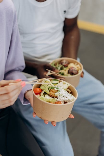 Two people holding paper bowls filled with salads, one person using chopsticks to eat.