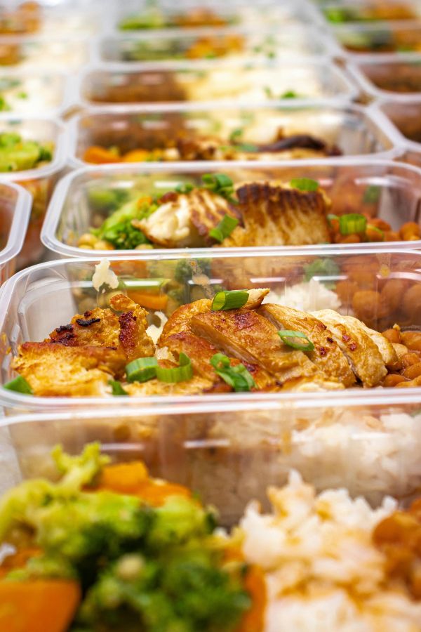 Rows of plastic meal prep containers filled with grilled chicken, rice, broccoli, and carrots, arranged neatly in a grid.
